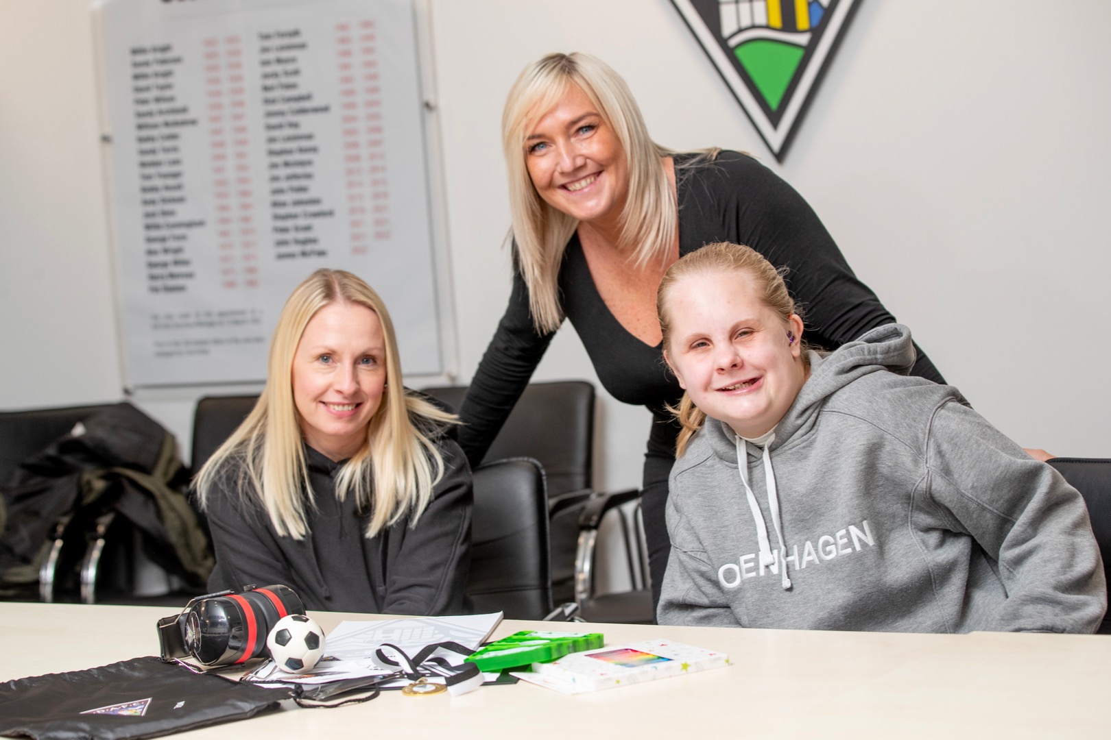 Three people are indoors, looking into the camera and smiling