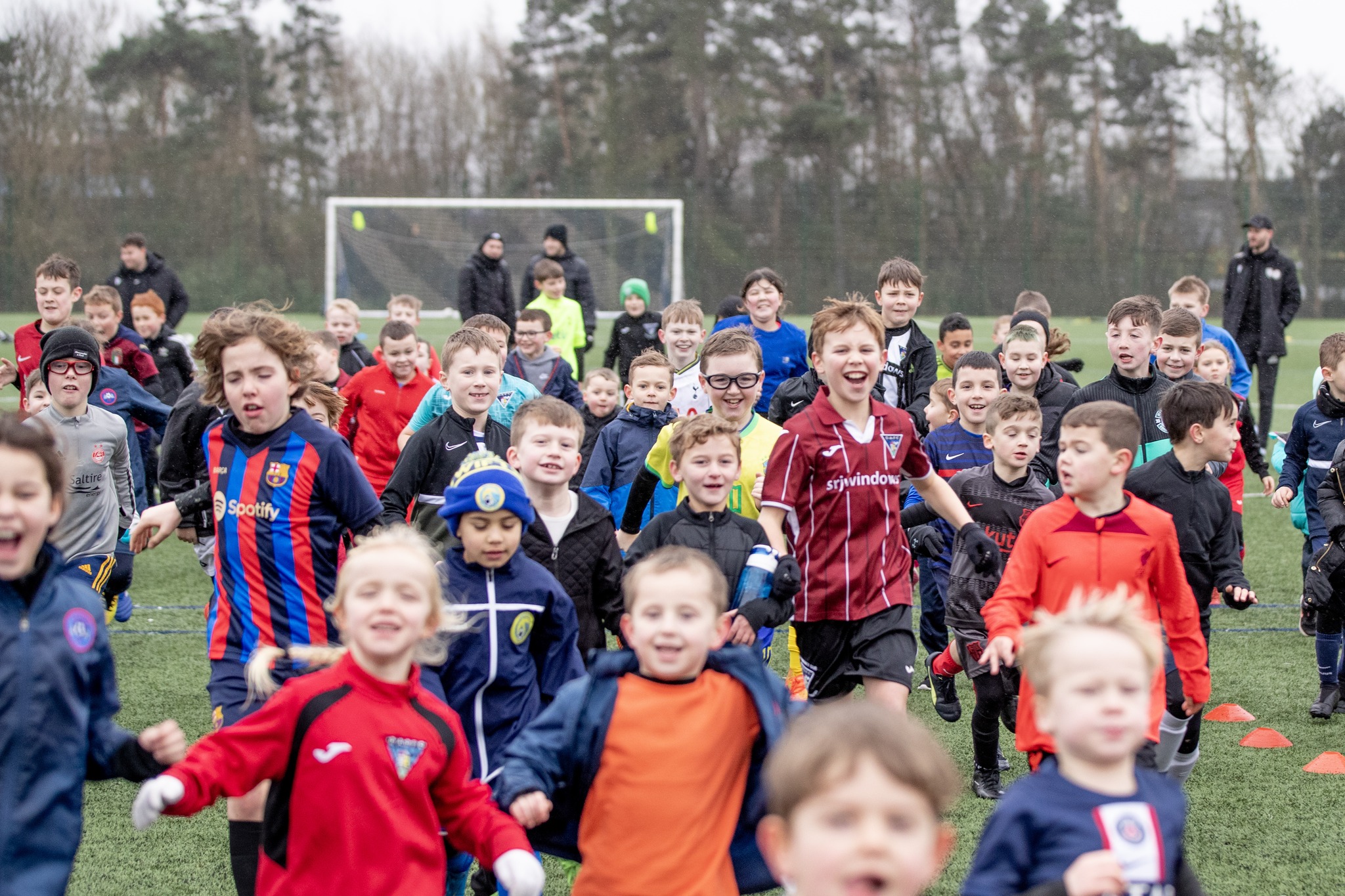 Large group of children on a football pitch, looking happy and running towards the camera
